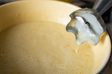 Batter or liquid dough for cooking a tasty pie in yellow metal dish (very shallow DOF) with blender