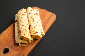 Homemade Norwegian Potato Flatbread (Lefse) with Butter and Sugar on a rustic wooden board on a black background, side view. Copy space.