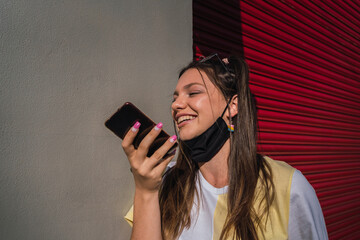 Portrait of a happy girl using voice recognition on a smartphone - Woman sends message with open face mask  - New normality concept