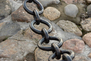Old forged rusty chain with peeling paint on the background of paving stones.