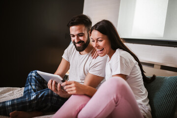 Smiling relaxed young couple using digital tablet in bed at home