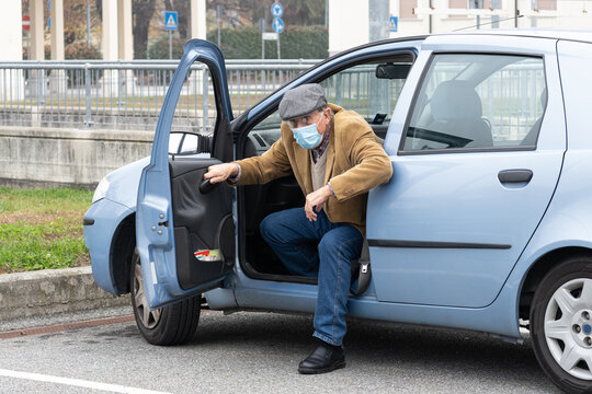 Elderly man with protective mask goes out with fatigue from his car. Concept of old age and difficulty of movement