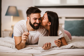 Young couple shopping online from the comfort of bedroom and using digital tablet and credit card