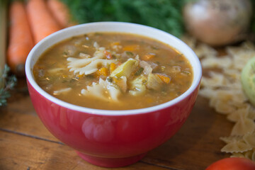 Minestrone soup, a typical thick vegetables soup, originally from Italy, served in a red bowl with Farfalle Pasta. 
