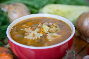 Minestrone soup, a typical thick vegetables soup, originally from Italy, served in a red bowl with Farfalle Pasta. 