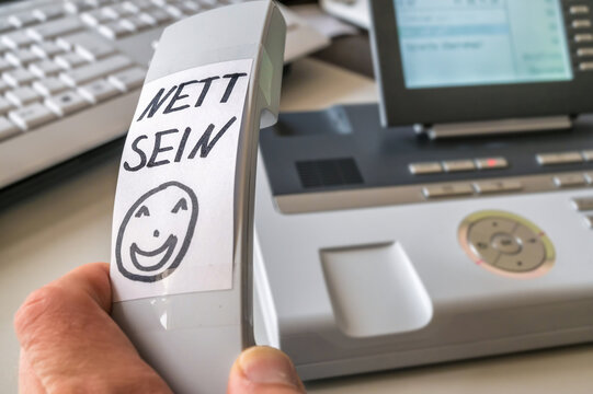 Vermerk "Nett sein" in deutscher Sprache auf dem Hörer eines Telefones zur Erinnerung an freundlichen Umgang mit dem Anrufer
