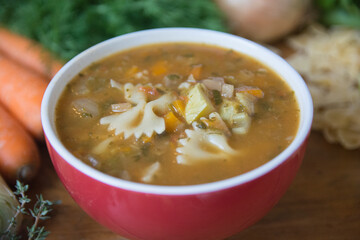 Minestrone soup, a typical thick vegetables soup, originally from Italy, served in a red bowl with Farfalle Pasta. 