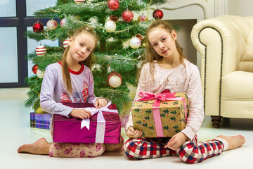 Obraz na płótnie Canvas Happy Girls in Pajamas Sitting on the Floor with Gift Boxes
