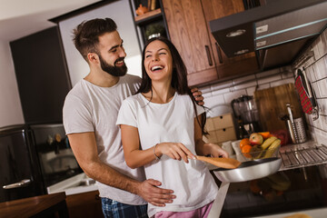 Woman preparing food at the stove with partner behind her in kitchen