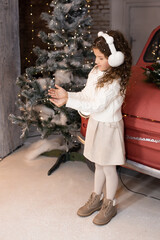 cute little girl playing with snow near red car and Christmas trees with lights. Merry Christmas and Happy Holidays