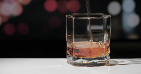 Pouring whiskey drink into glass on dark background