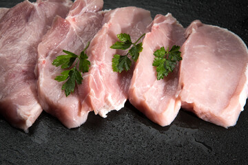 Raw slices of pork on cutting board and vegetables.