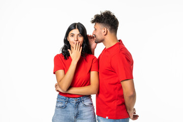 Naklejka premium Portrait of an astonished young couple telling secrets standing together over white background