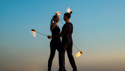 Sexy couple in love dance while spinning burning poi blue sky outdoors, fire show