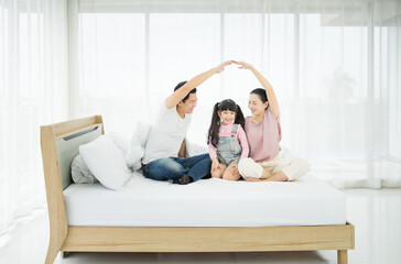 Young asian family ,dad mom and daughter being playful on bed at home.