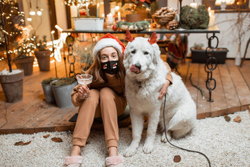 Young woman in facial mask celebrating with a dog New Year holidays at home. Concept of quarantine and self-isolation during the epidemic on holidays