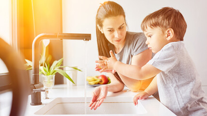 Child learning to wash hands with mother at the sink