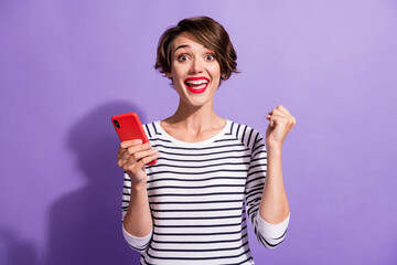 Photo of excited pretty girl hold telephone raise fist wear striped shirt isolated violet color background