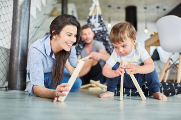 Mother helps child play tent and stack wood