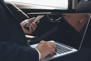 Businessman working on laptop computer and using mobile phone inside  a car