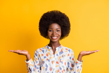 Photo of pretty dark skin woman wear casual outfit spectacles holding two arms palms empty space isolated yellow color background