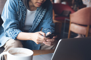 Casual woman using mobile phone online working on laptop computer in coffee shop