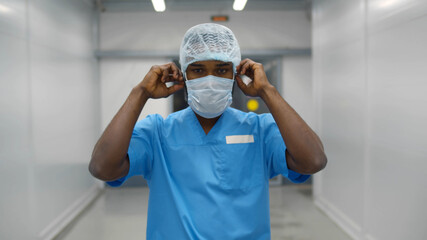 Fototapeta na wymiar Young male afro doctor wearing scrubs and cap walking along hospital corridor