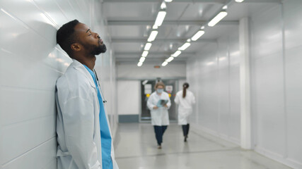 Tired male african doctor standing in hospital corridor