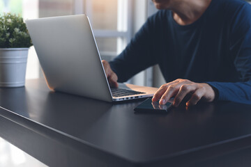 Casual man working on laptop computer and using mobile smart phone on office table at home