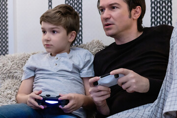 Mid adult man playing video games with his son at home.