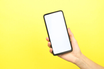 Female hand holding a phone with a white screen on a yellow background