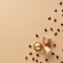 Caffeine, hot drinks and objects concept - close up of golden capsules or pods for coffee mashine with some roasted grains on beige background. Top view with space for text. Flat lay..