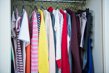 Colorful clothes on hangers in well organized wardrobe at home. Choice of cotton clothes of different colors on hangers. Organizational space - management of environment.