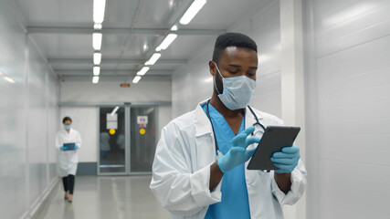 African doctor wearing protective mask and gloves using tablet working in clinic
