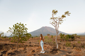 Adventurous young woman in jeans and white t-shirt looks at the mountains in the distance. Agung...