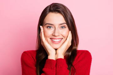 Closeup headshot photo portrait of cute pretty young girl touching cheeks with both hands smiling wearing red sweater isolated on pink color background