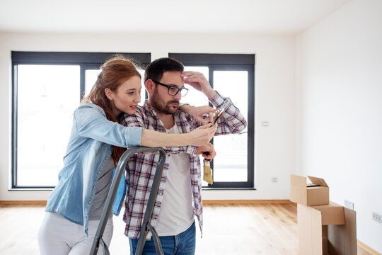 Couple In New House Plan How To Paint Walls And Looking At Samples Of Colours With Brushes On Hand