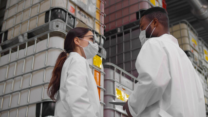 African and caucasian inspectors in safety mask and lab coat standing in chemical factory warehouse