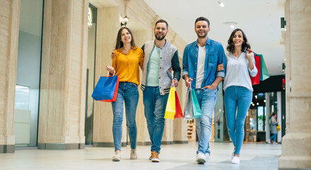 Happy group of excited beautiful modern stylish friends in casual wear with paper bags are walking in the mall during shopping.