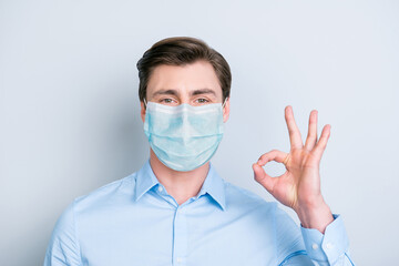 Close-up portrait of content guy wearing safety gauze mask disease prevention showing ok-sign isolated on gray color background