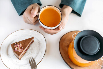 A woman sits at a white table with sea buckthorn tea, a slice of cake. View from above