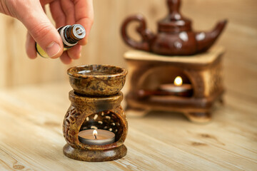 Hand of therapist pours drops of essential oil to a ceramic diffuser in spa salon