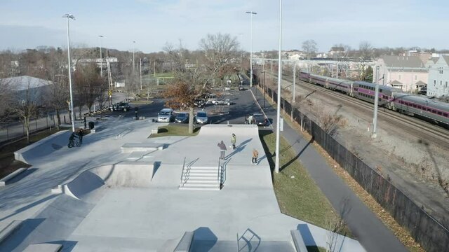 Skateboarders riding Hyde skatepark with train passing ,drone aerial, Boston Massachusetts