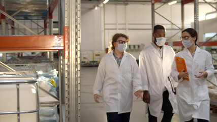 Industrial engineers in lab coat and safety mask walking in large warehouse