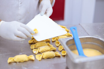 Gloved woman’s hands arranging handmade pasta, using a dough card.
