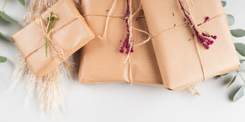 Zero waste holiday gifts wrapped in plastic free paper with dried floral decor on gray background.