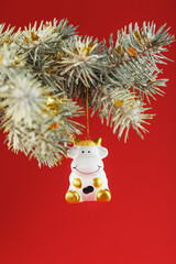 Figure of a Cow on a spruce branch, on a red background.