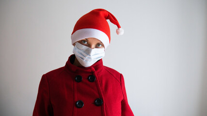 A woman in a red coat, a Santa hat and a medical mask on her face. Christmas and New Year in the season of flu and pandemic coronavirus.