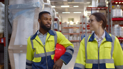 Diverse engineers holding safety helmet and chatting walking in industrial warehouse