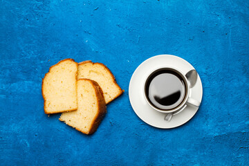 Una taza de café junto a unos trozos de bizcocho sobre una mesa un fondo azul clásico y rústico. Vista superior. Copy space